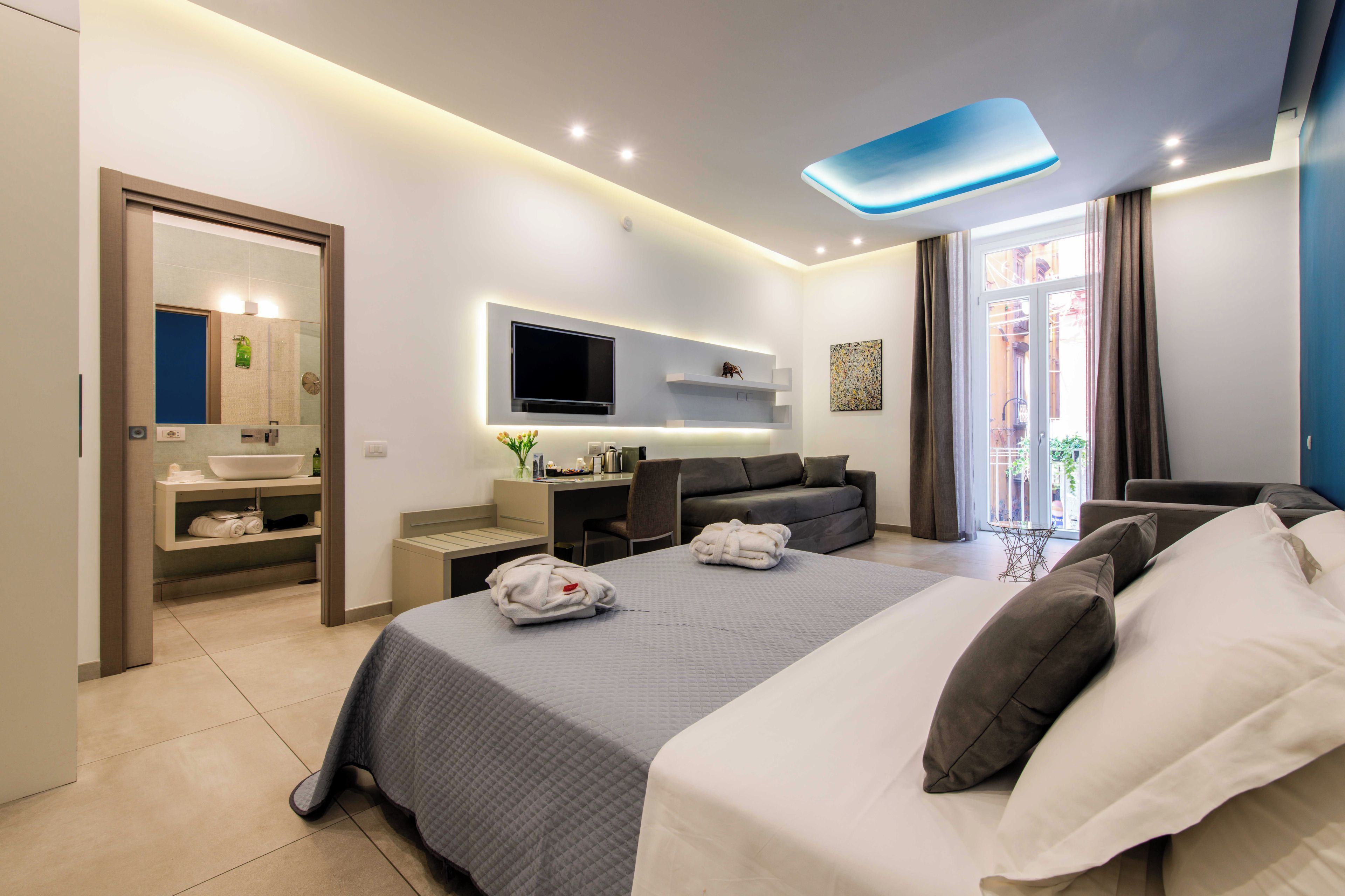 A modern hotel room with a large bed, a flat-screen TV, a desk, and a seating area.