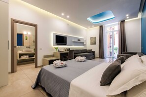 A modern hotel room with a large bed, a flat-screen TV, a desk, and a seating area. - Toledo 16 Luxury Suites (Naples)