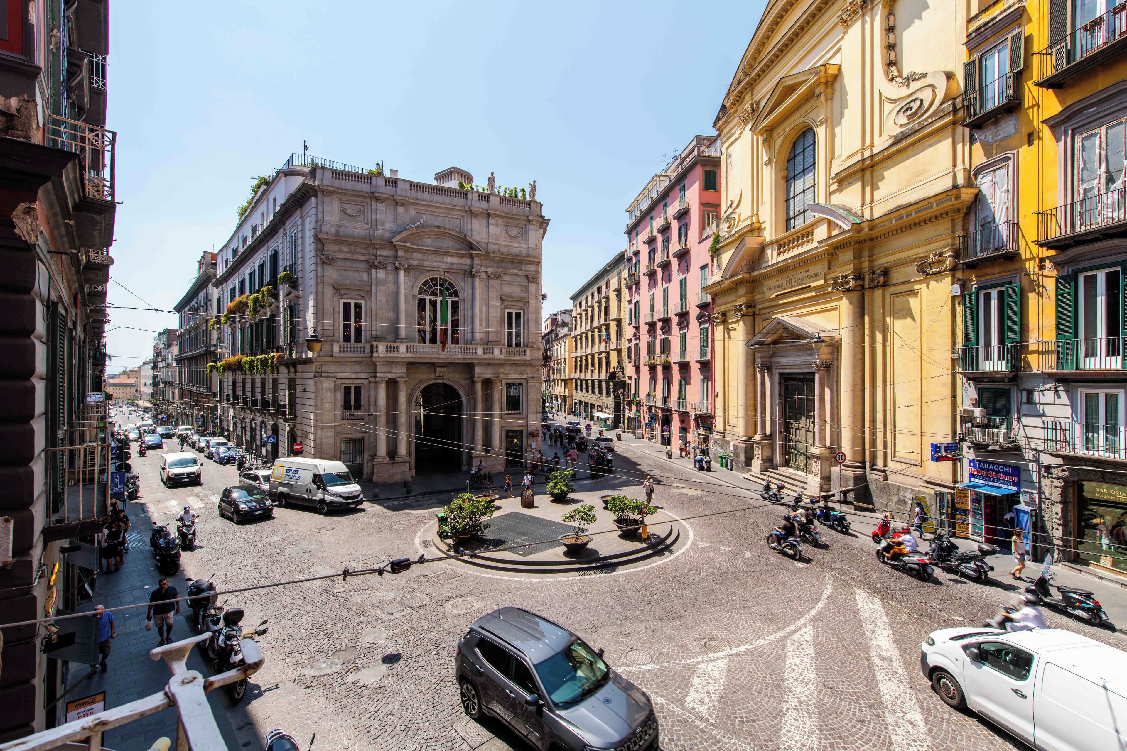 Una calle empedrada con edificios históricos, una glorieta y vehículos estacionados.