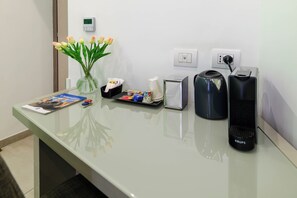 A hotel reception desk with a vase of flowers, a magazine, a tray of snacks, a coffee maker, and a kettle. - Toledo 16 Luxury Suites (Naples)