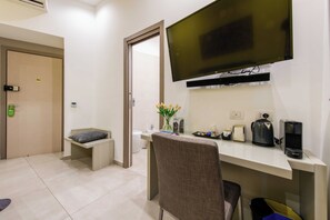 A hotel room with a desk, chair, television, and a coffee machine. - Toledo 16 Luxury Suites (Naples)