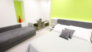 A modern hotel room with a bed, a grey sofa, a desk, and a bright green accent wall. - Toledo 16 Luxury Suites (Naples)