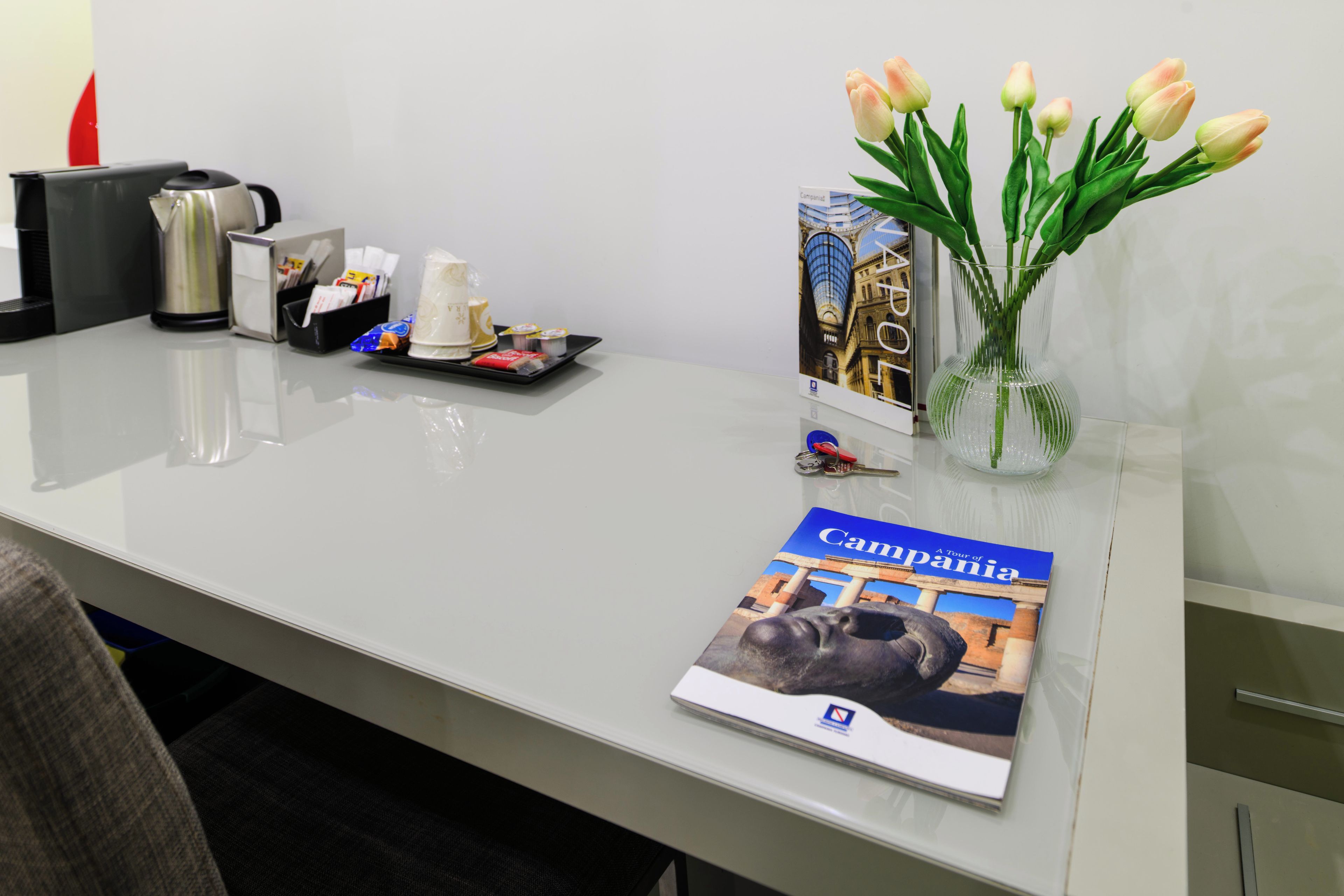 Een bureau met een brochure, een vaas met tulpen, een dienblad met snacks en een koffiezetapparaat.
