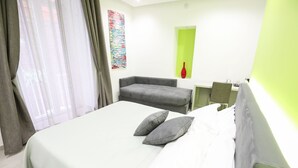 A hotel room with a bed, a grey sofa, a small table, and a green accent wall. - Toledo 16 Luxury Suites (Naples)