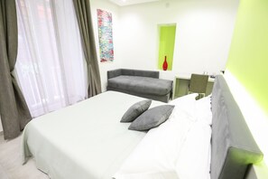 A hotel room with a bed, a grey sofa, a small table, and a green accent wall. - Toledo 16 Luxury Suites (Naples)