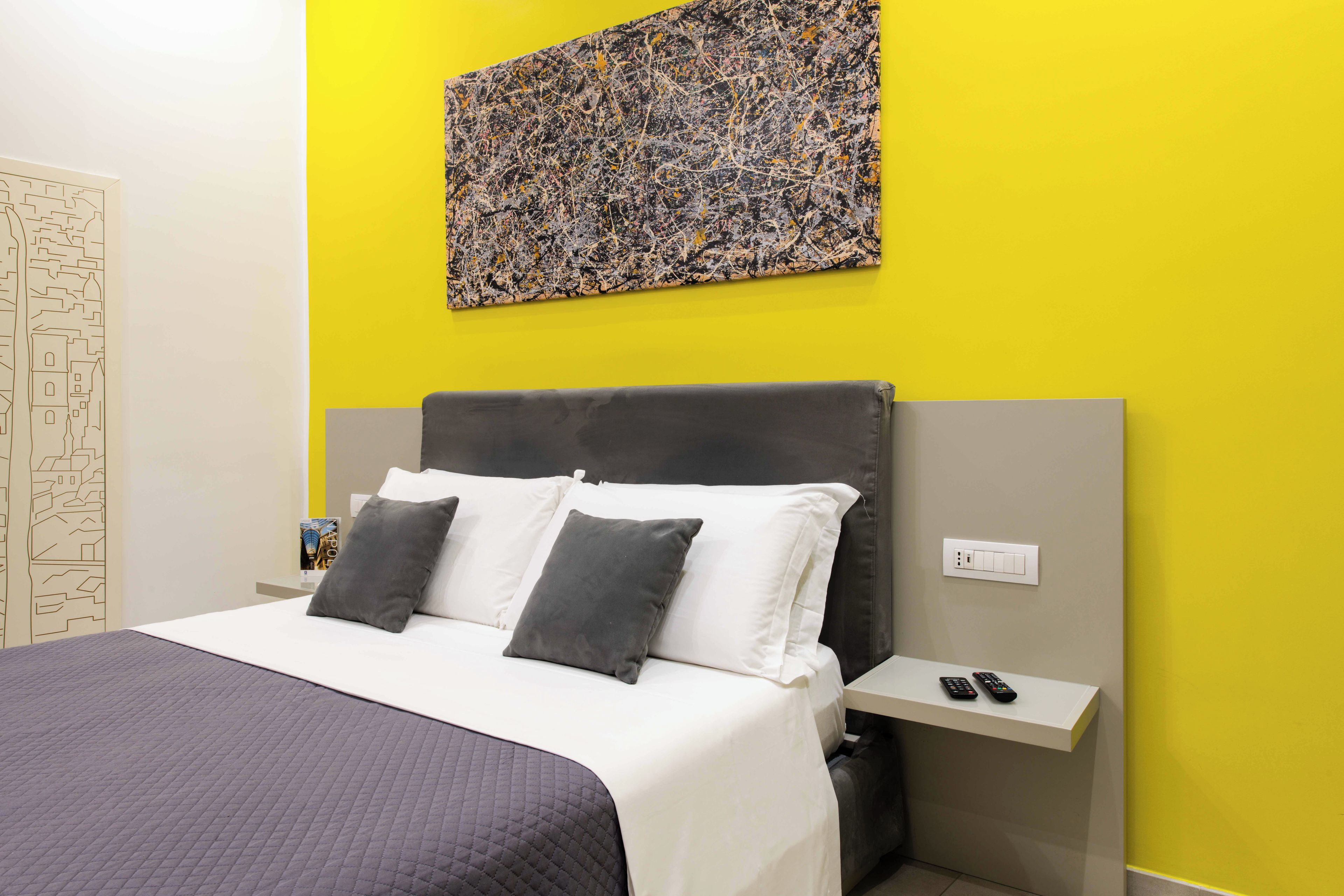Habitación de hotel con cama, mesita de noche, un cuadro colgado en la pared y una pared con diseño geométrico.