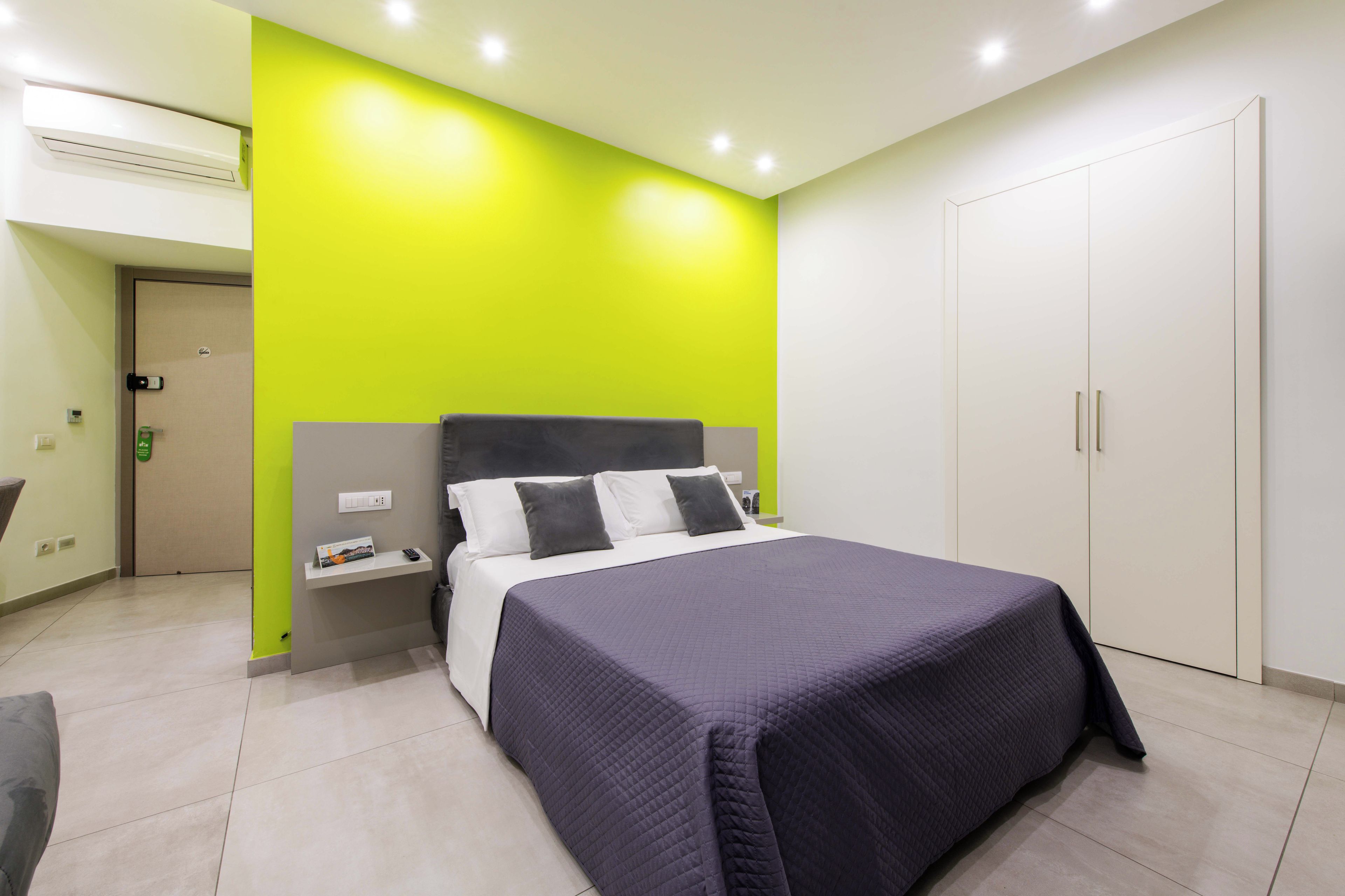 A hotel room with a bed, a nightstand, a wardrobe, and a bright green accent wall.