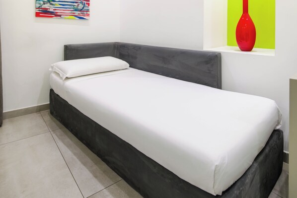 A single bed with a white mattress and gray headboard in a room with a tiled floor. - Toledo 16 Luxury Suites (Naples)
