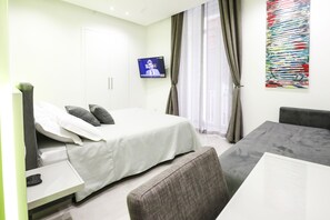 A modern hotel room with a bed, a desk with a computer, a TV mounted on the wall, and a large abstract painting. - Toledo 16 Luxury Suites (Naples)