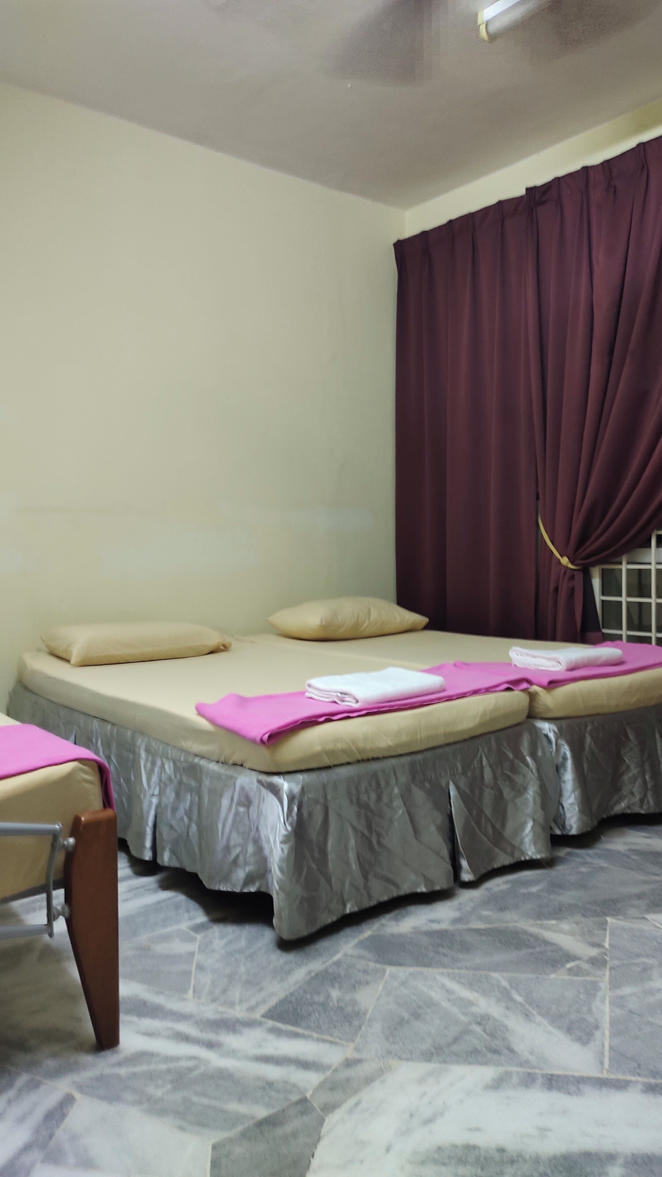 A room with a bed, a chair, a window with curtains, and a tiled floor.