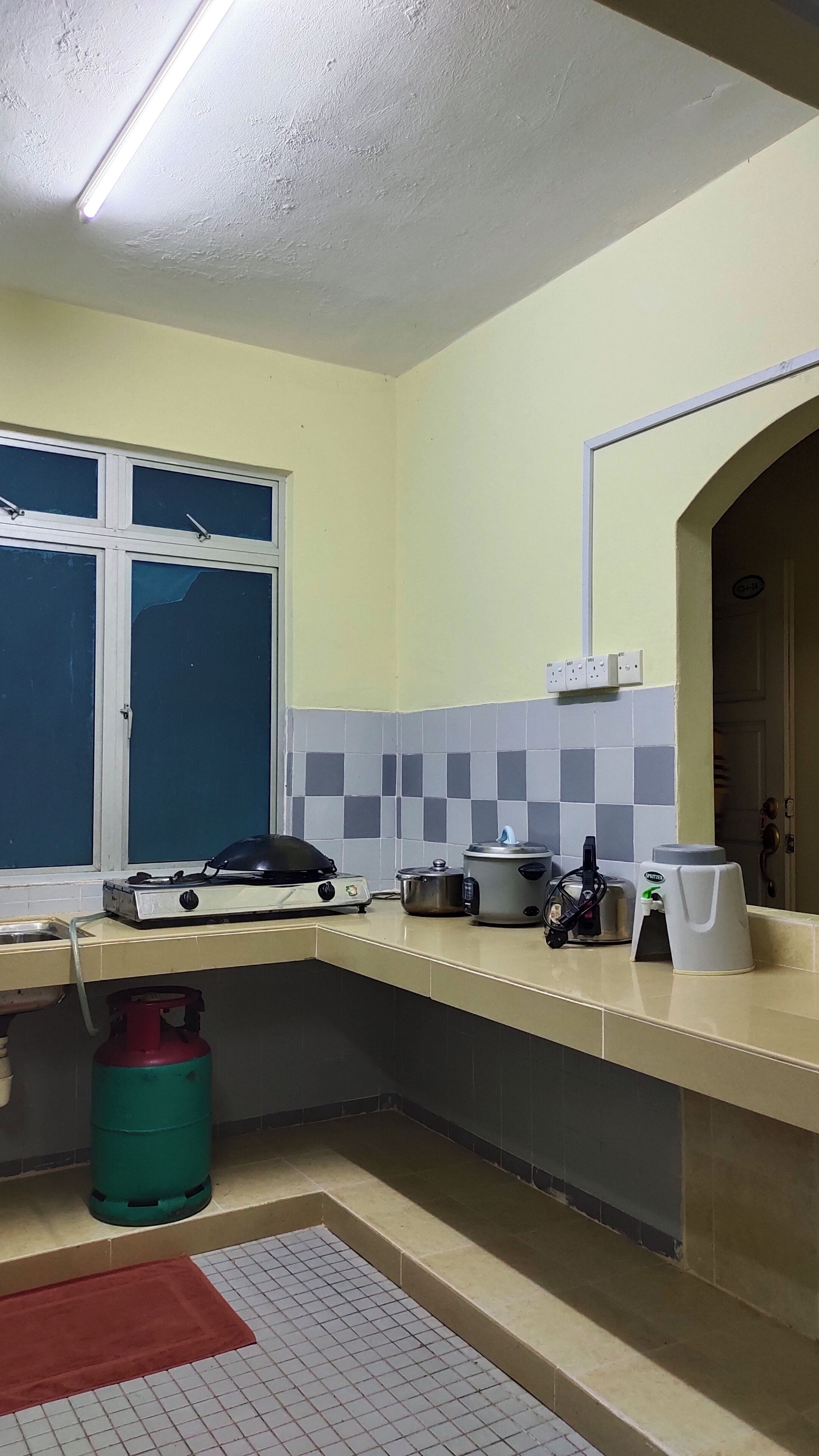 Una cocina con estufa a gas, cilindro de gas, lavamanos y ventana con vistas.