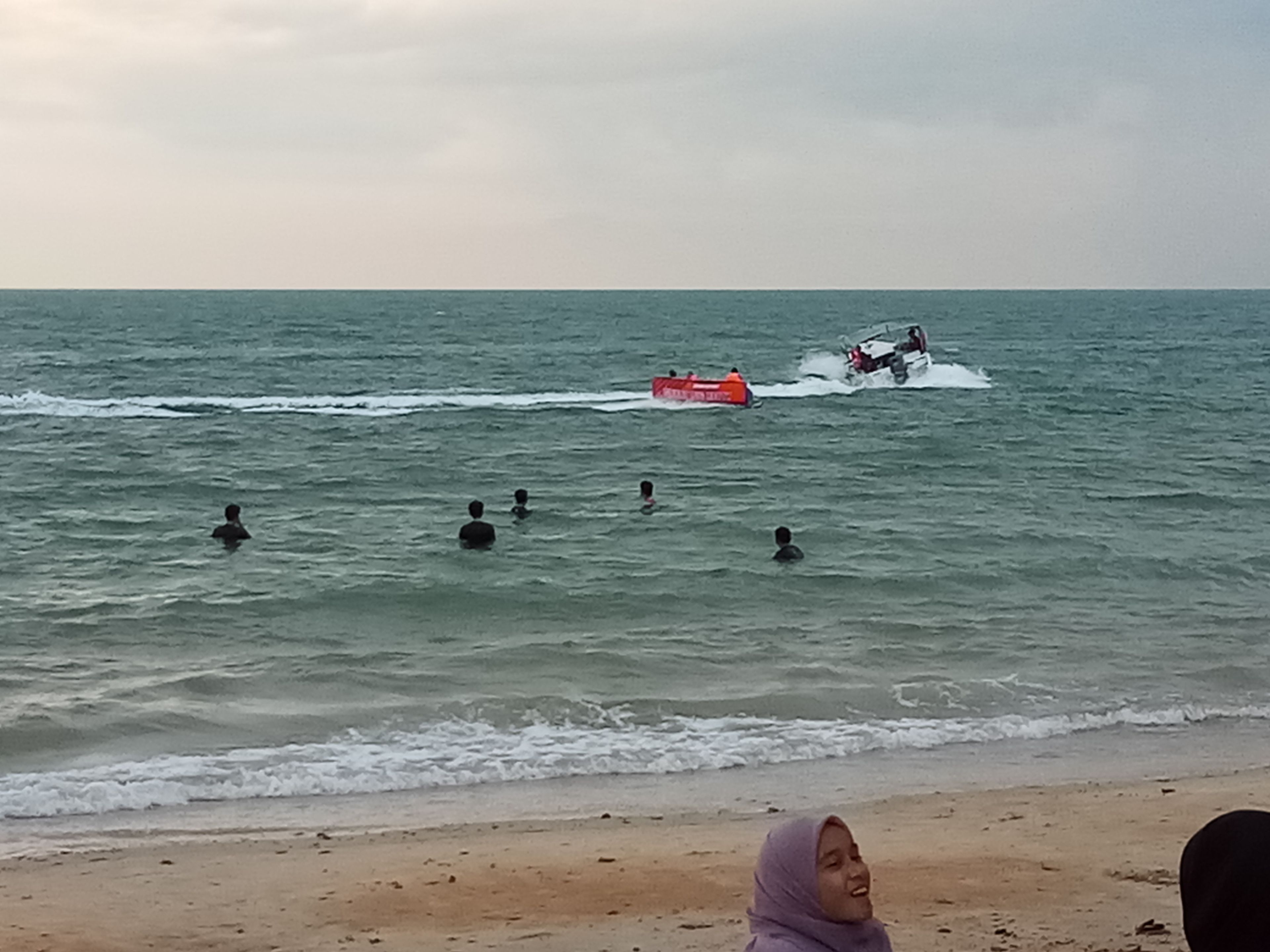 Una playa con gente nadando y un jet ski en el agua.