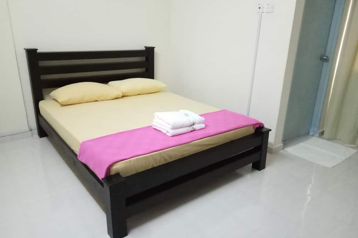Een eenpersoonsbed met een zwart frame, beige beddengoed en een roze deken.