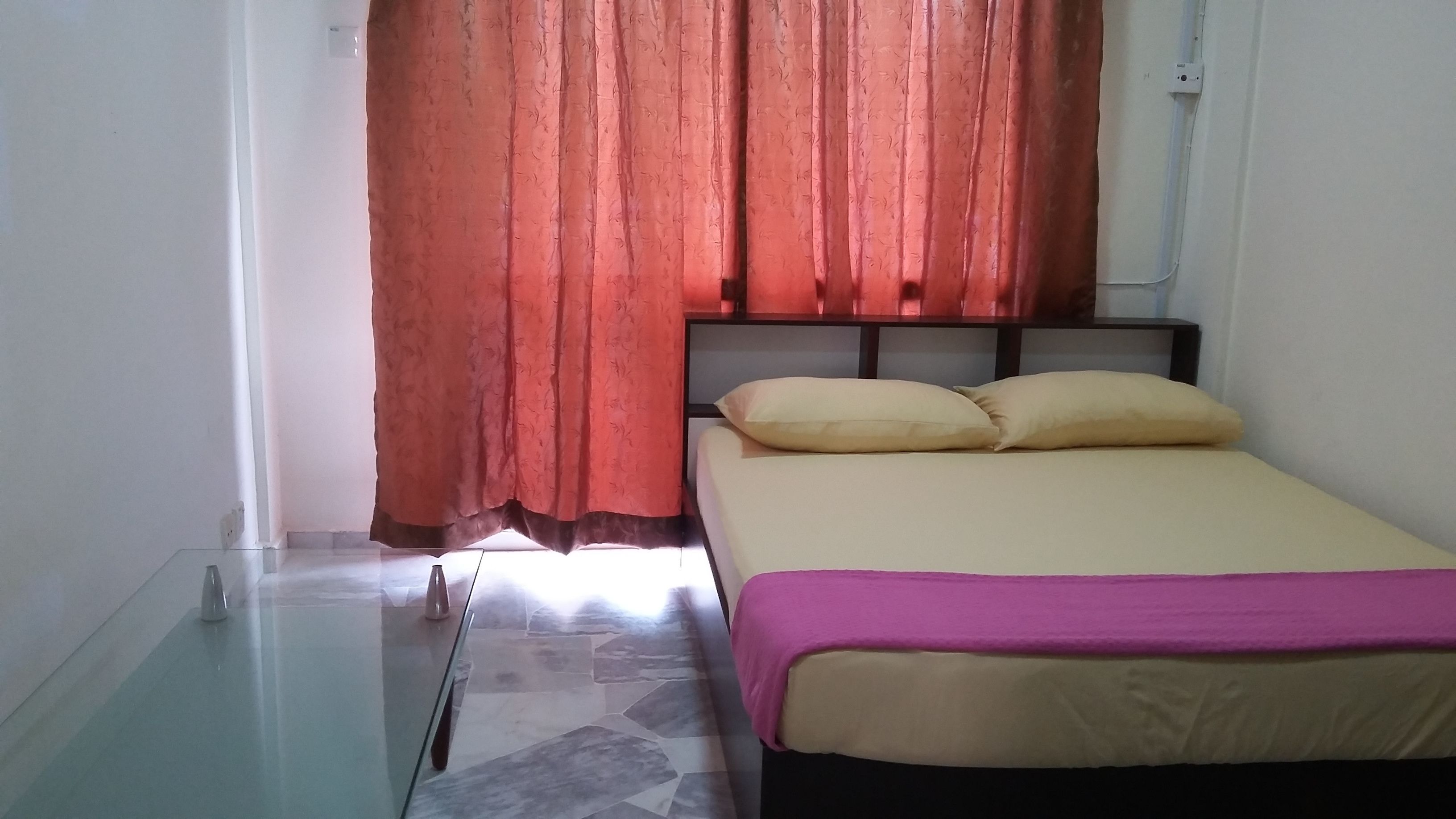 Une chambre à coucher avec un lit, une table en verre, un rideau rouge et un sol carrelé.