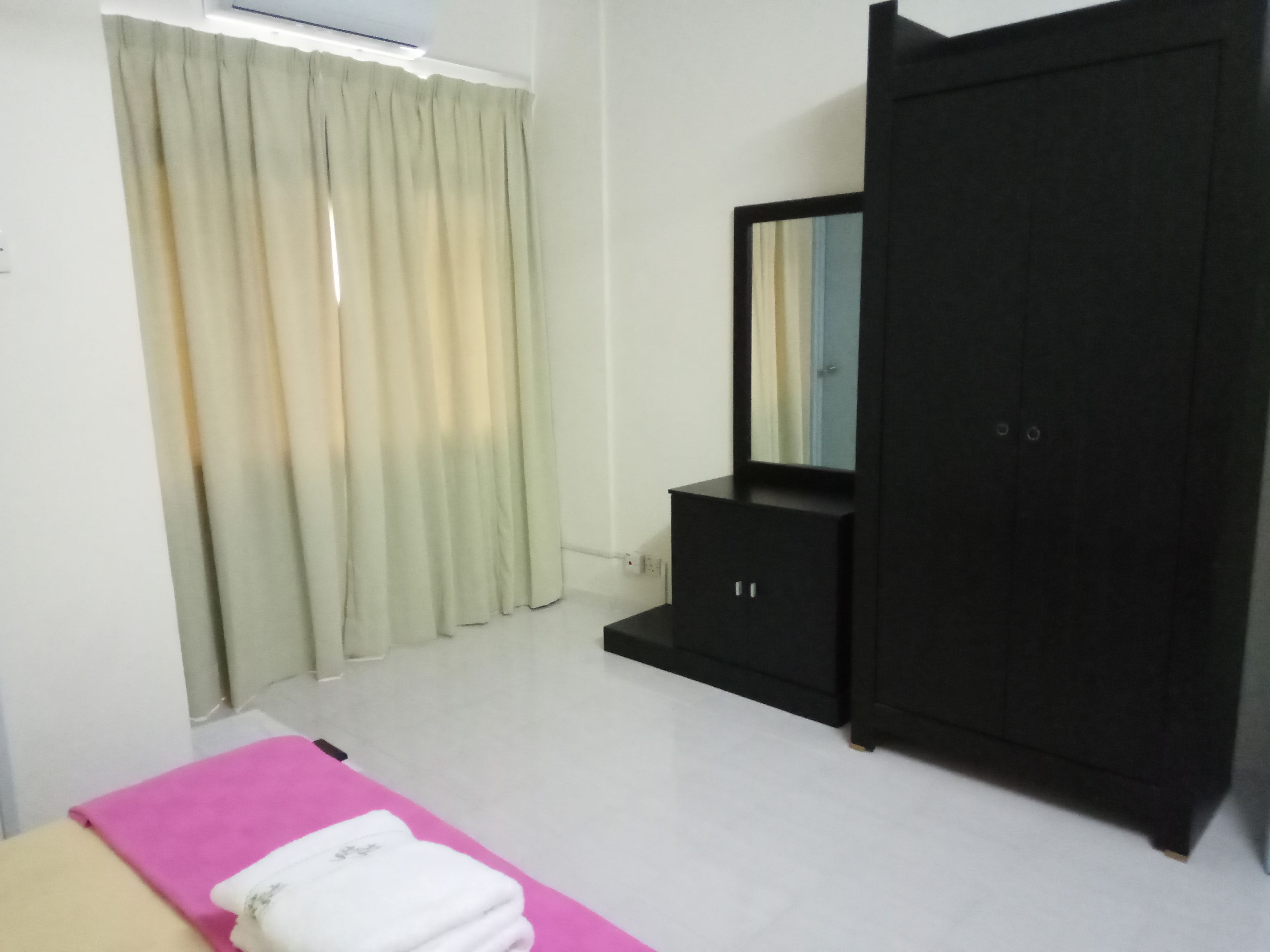 A bedroom with a bed, a wardrobe, a mirror, and a window with curtains.