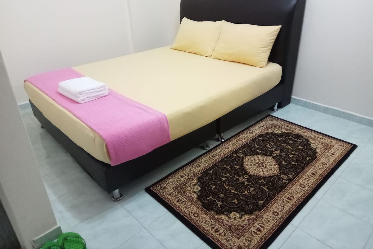 Een bed met een zwart hoofdeinde, een roze deken en een beige matras.