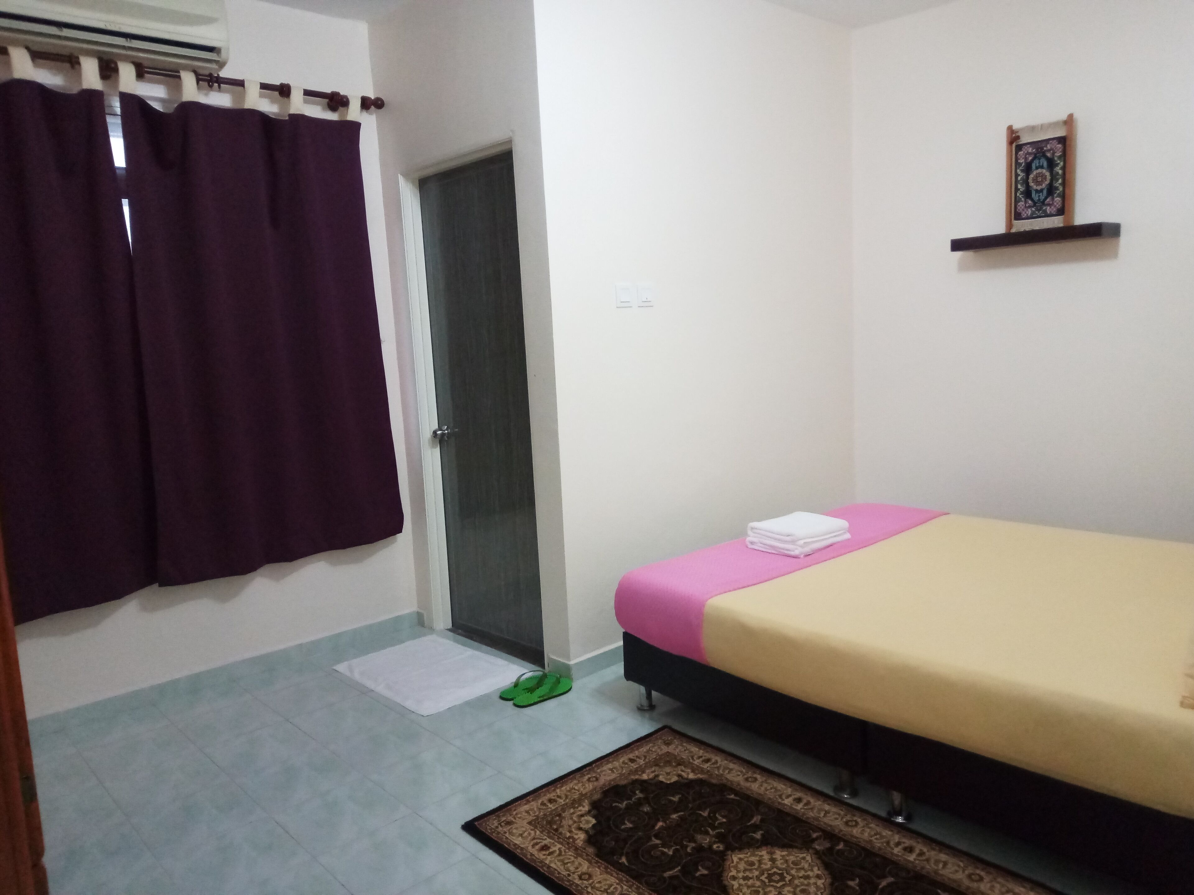 Un dormitorio con cama, una puerta, un tapete pequeño y un estante fijado a la pared.