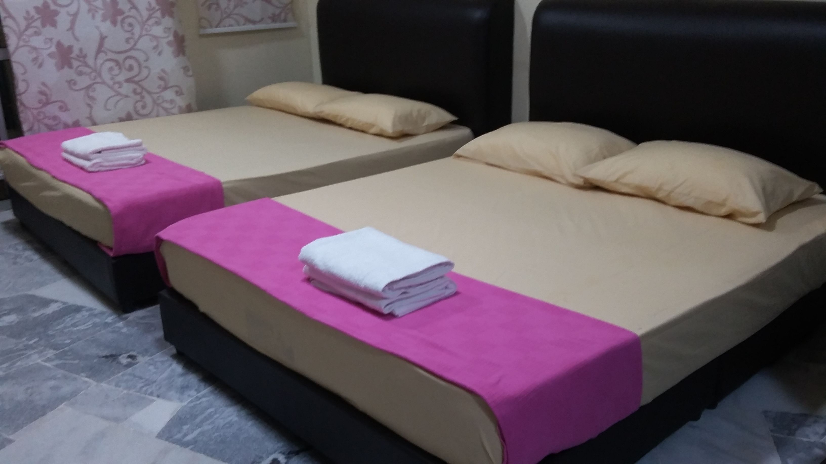 Dos camas individuales con ropa de cama rosa y beige, almohadas y toallas blancas dobladas.