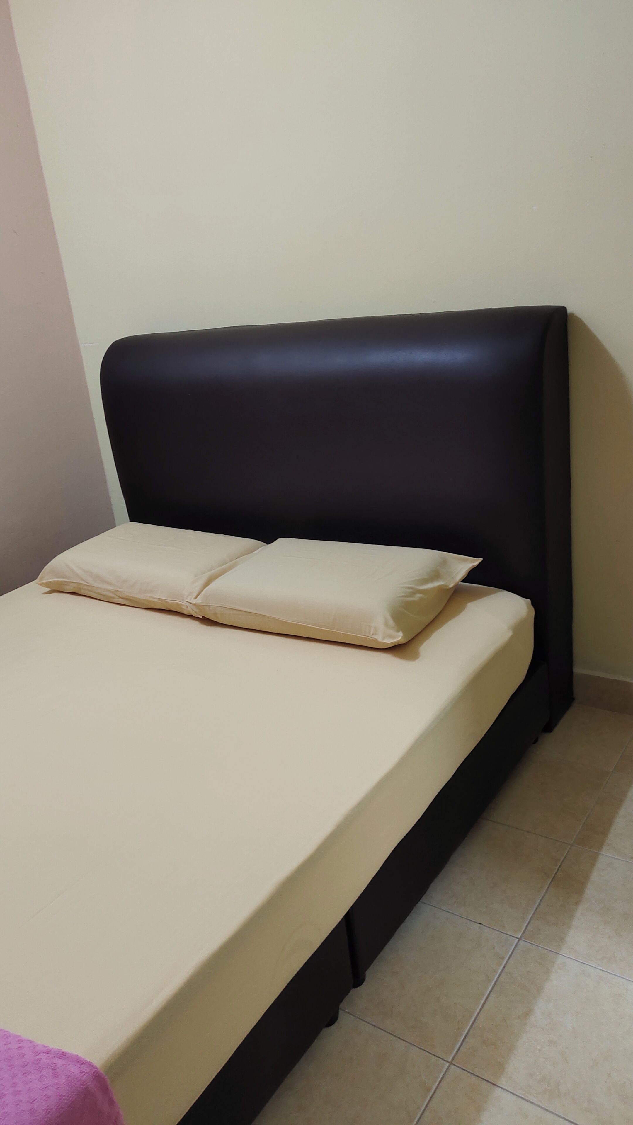 Un letto con una testiera nera, biancheria beige e una coperta rosa.
