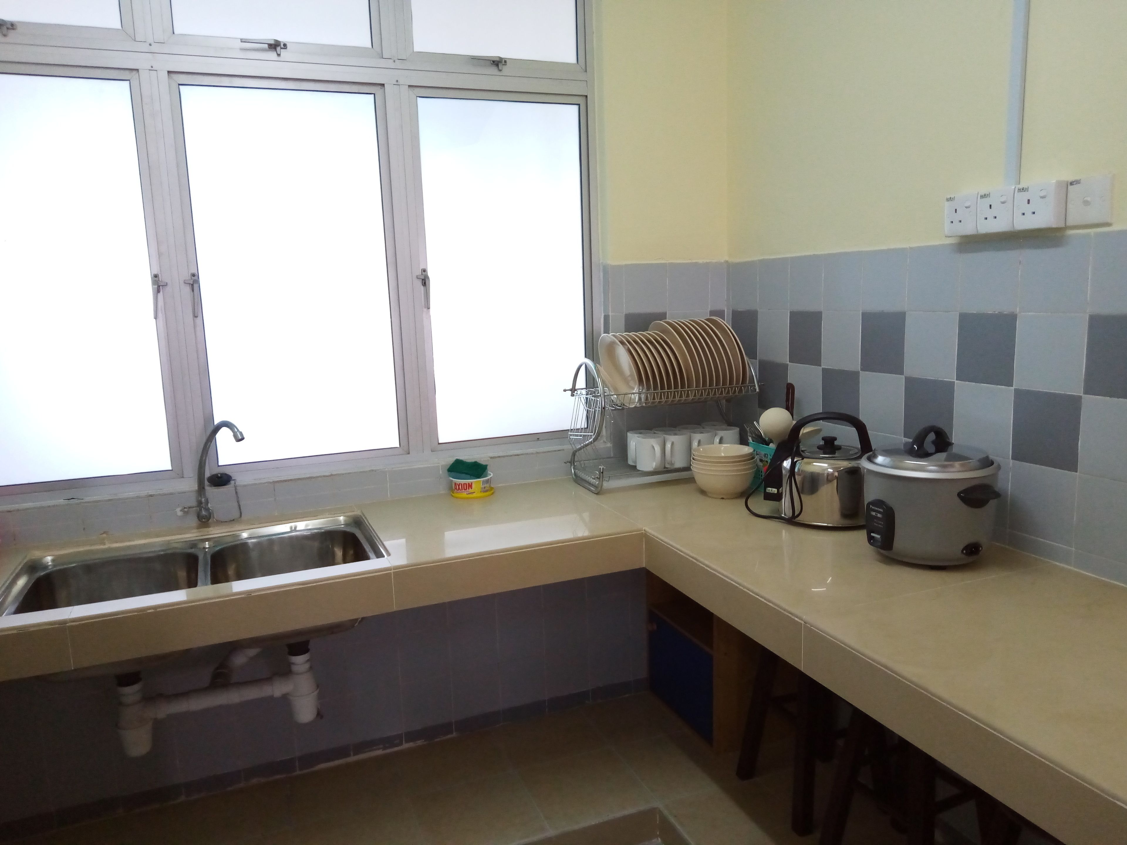 Una cocina con ventana, un fregadero, un escurreplatos, un hervidor y una olla de cocción lenta.