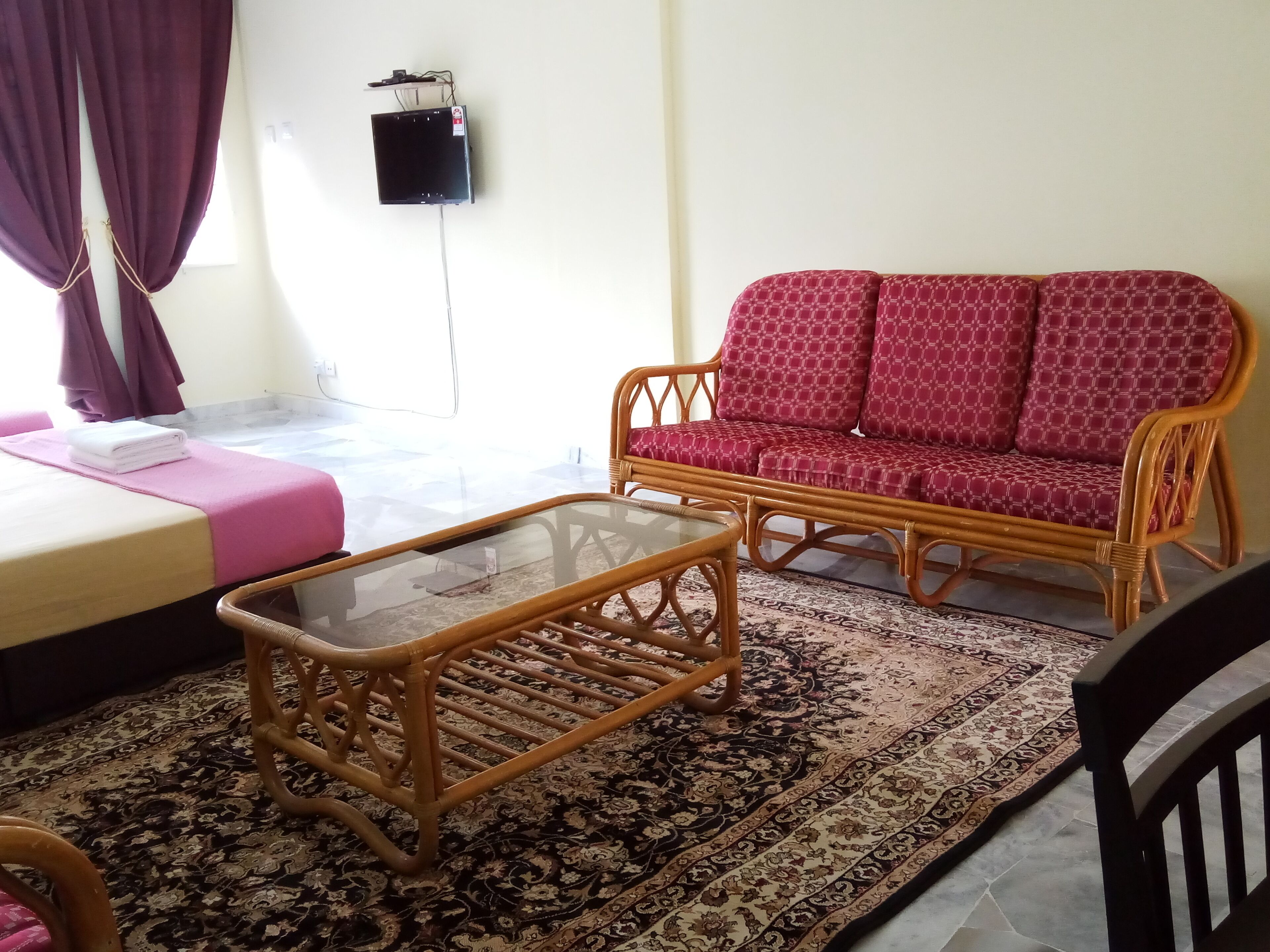 A room with a bed, a sofa, a glass-top coffee table, and a patterned rug.