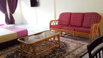 A room with a bed, a sofa, a glass-top coffee table, and a patterned rug.