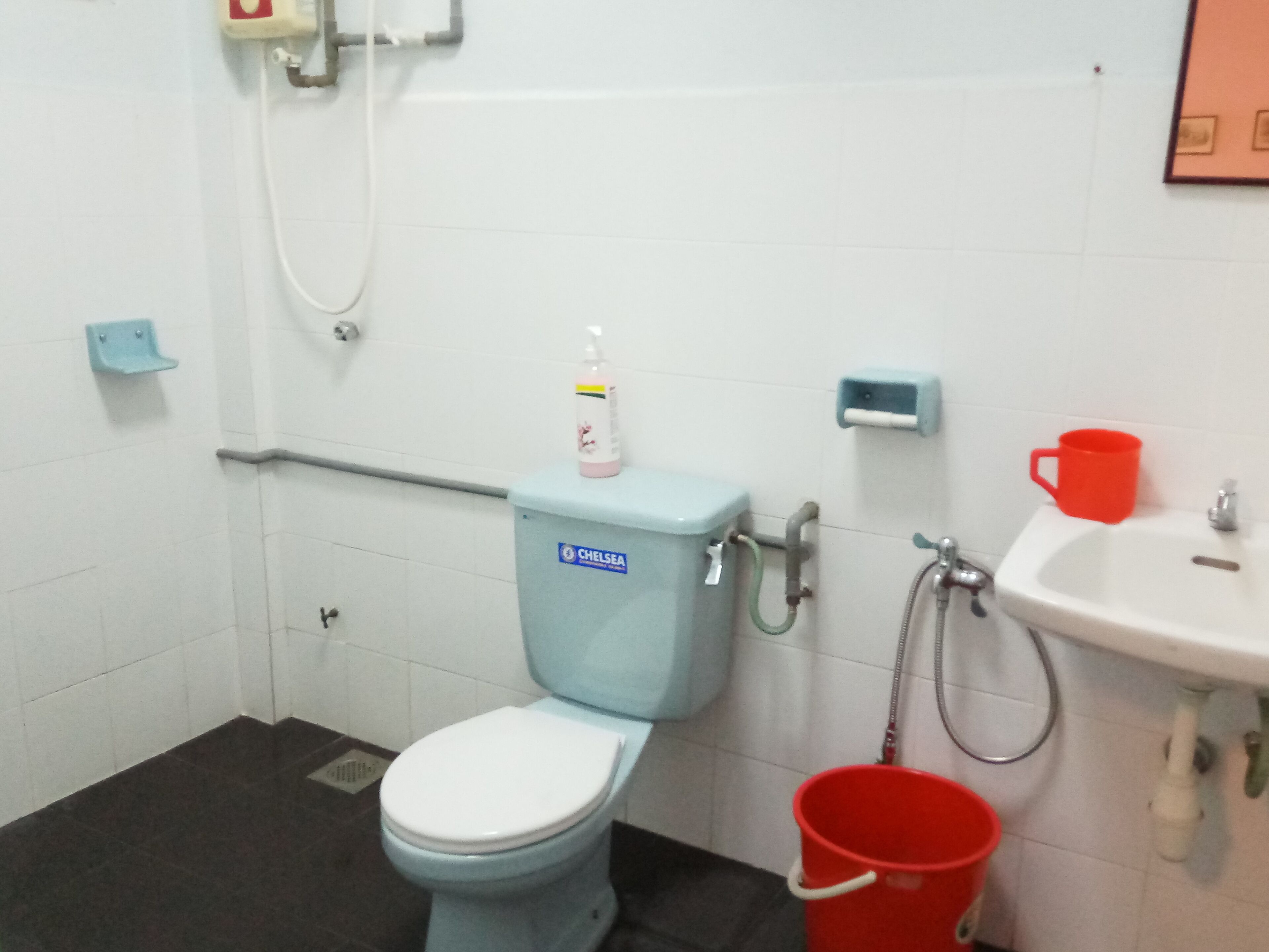 A bathroom with a toilet, a sink, and a red bucket.