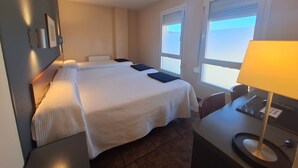 A hotel room with a bed, bedside tables, a desk with a lamp, and windows with blinds. - Hotel Yerri (Estella)