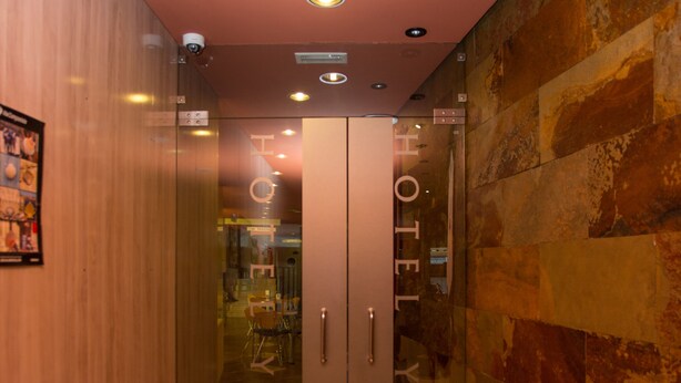 A hotel interior with a modern design, featuring a glass door entrance, a wooden wall on one side, and a textured stone wall on the other. - Hotel Yerri (Estella)