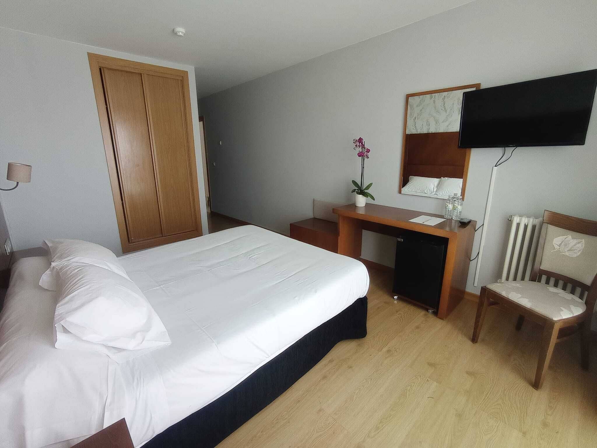 Una habitación de hotel con cama, escritorio, silla, televisor y armario.