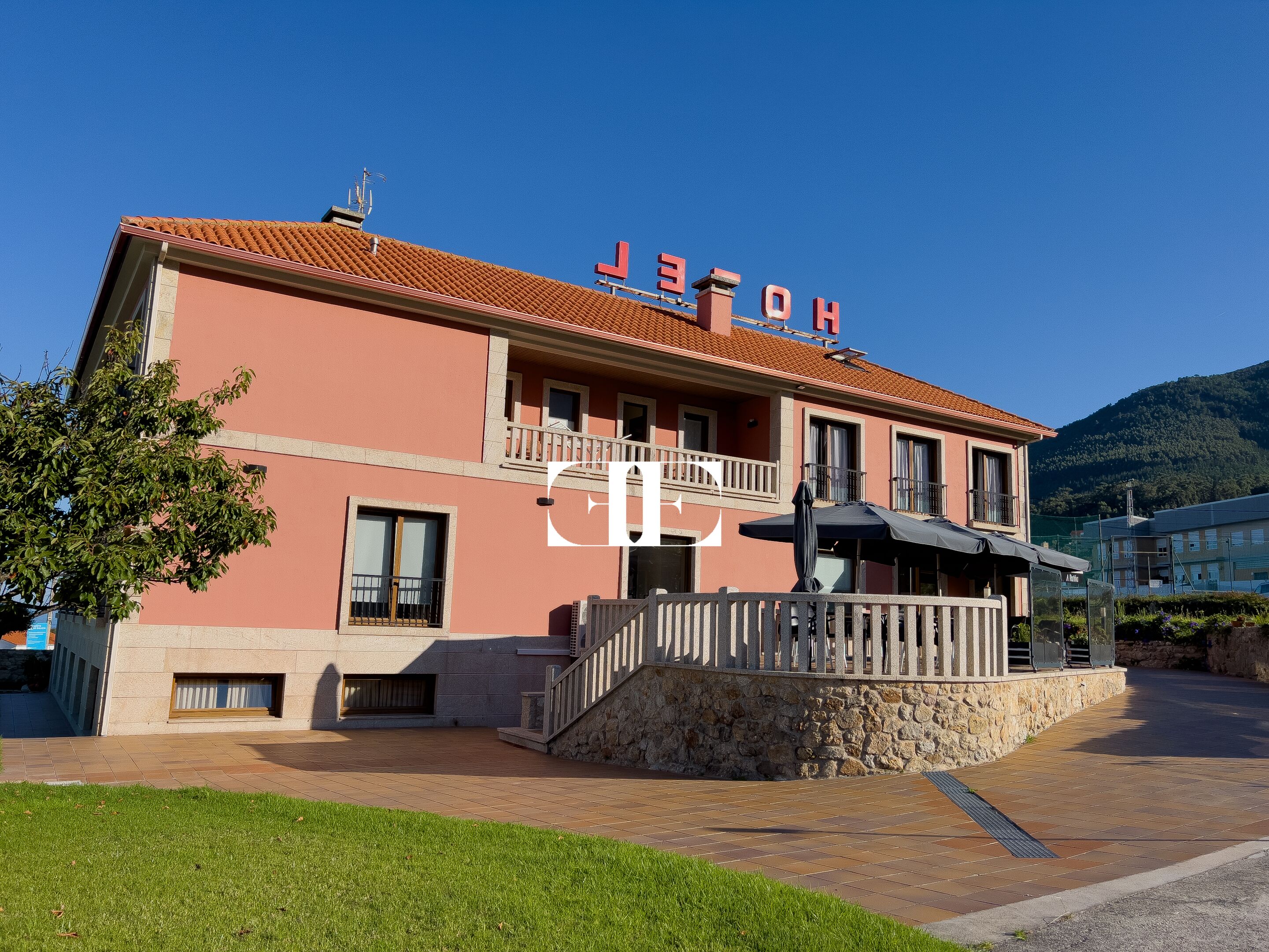 A hotel with a red facade, a balcony, and a stone wall in front.