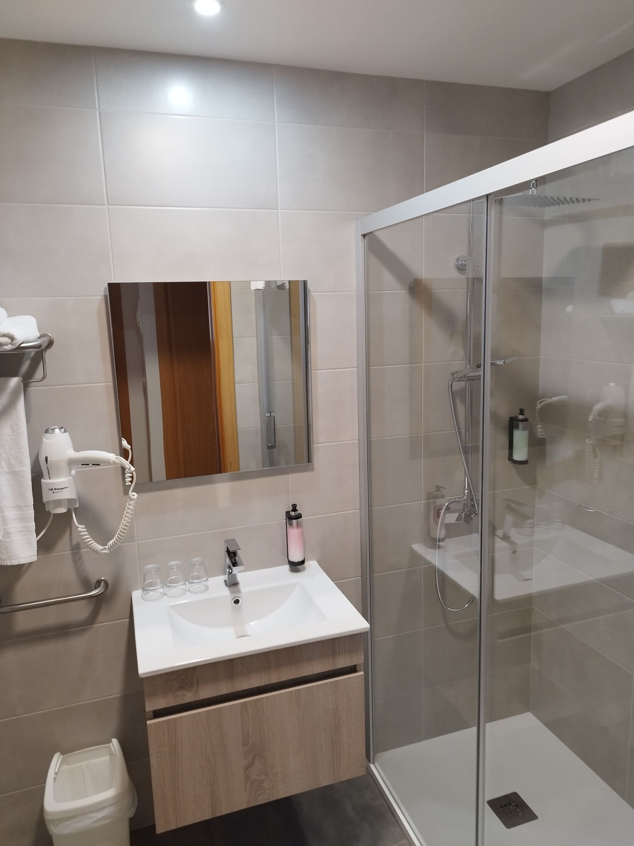 Ein modernes Badezimmer mit einer gläsernen Duschkabine, einem weißen Waschbecken und einem an der Wand befestigten Föhn.