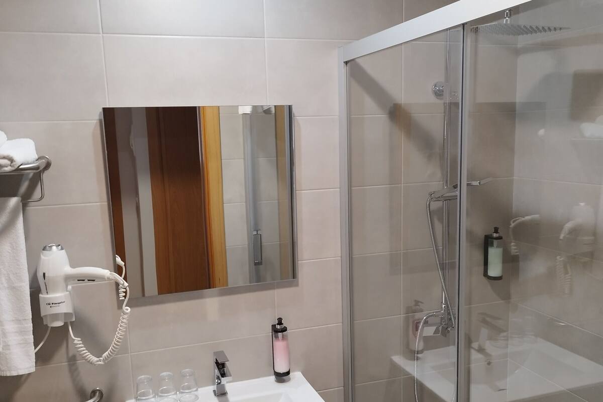 A modern bathroom with a glass-enclosed shower, a white sink, and a hairdryer on the wall.