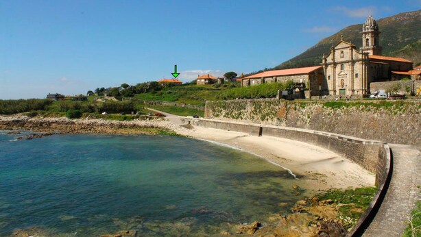 Eine Küstenlandschaft mit einem klaren Strand, einer Steinmauer und einer Kirche mit einem Glockenturm.