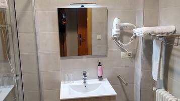 A modern bathroom with a glass shower enclosure, a white sink with a wooden vanity, a towel rack, and a hairdryer.