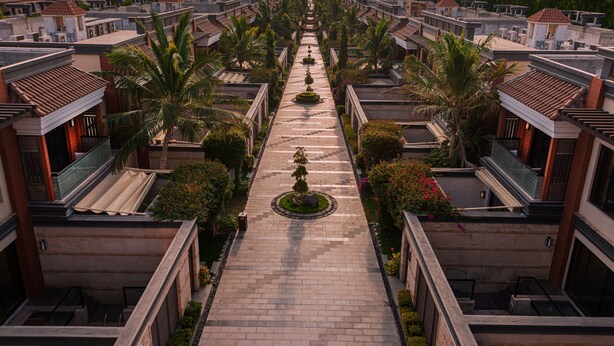 Disposizione simmetrica di edifici con un viale centrale, circondati da vegetazione e palme.