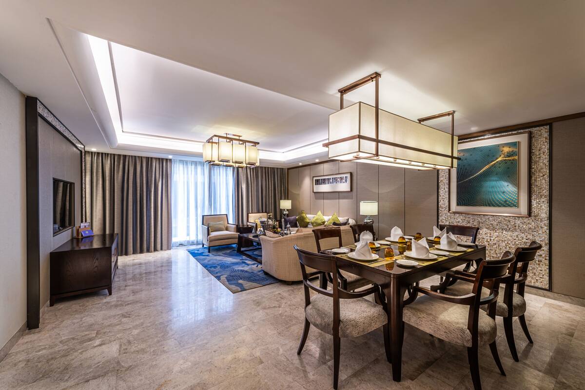 Une chambre d’hôtel moderne dotée d’un coin repas, d’un canapé, d’une télévision et d’un grand tableau au mur.
