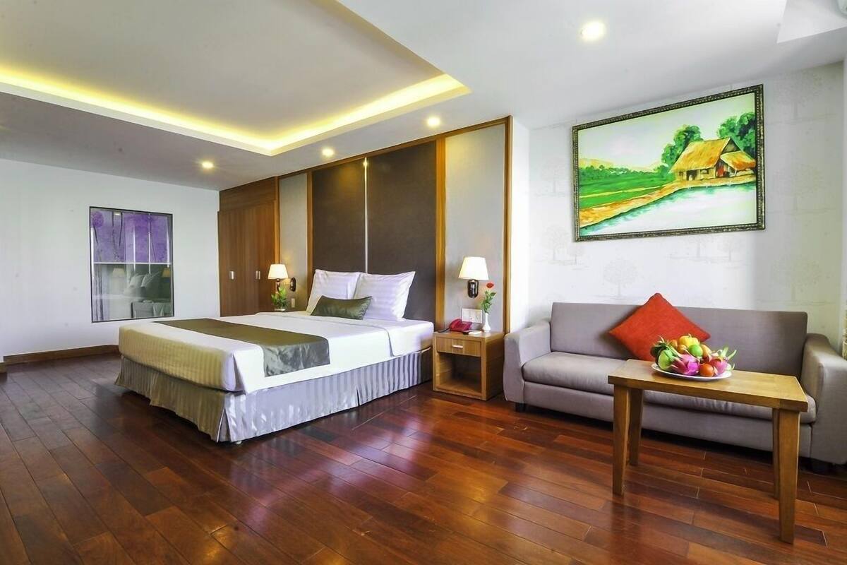 A hotel room with a large bed, a sofa, a small table with fruit, and a painting on the wall.