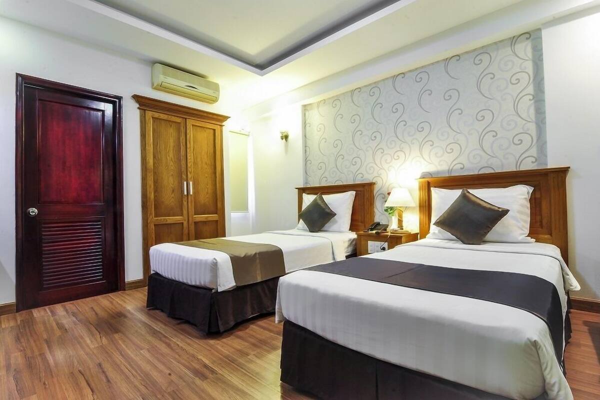 A hotel room with two beds, wooden wardrobe, and a patterned wallpaper.
