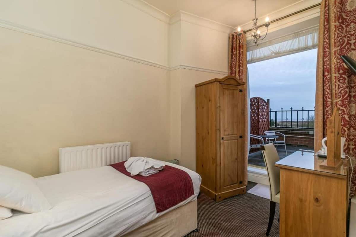 Une chambre d’hôtel avec un lit, une armoire en bois, un bureau avec une chaise et une vue sur le balcon extérieur.