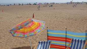 A beach with two striped beach chairs and a colorful umbrella.