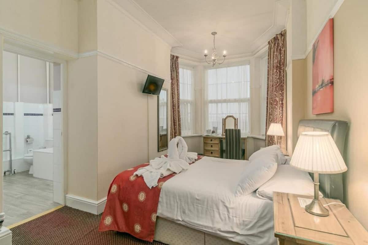 Une chambre d’hôtel avec un lit, une table de chevet avec une lampe, un miroir et un téléviseur fixé au mur.