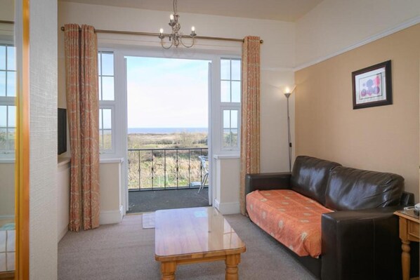 A living room with a leather sofa, a wooden table, and a balcony with a view of the countryside. - Skegness The Royal Hotel (Skegness)