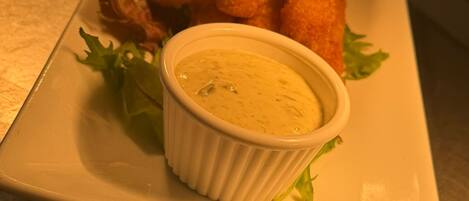 A plate with a rolled appetizer, a small bowl of dip, and some greens.