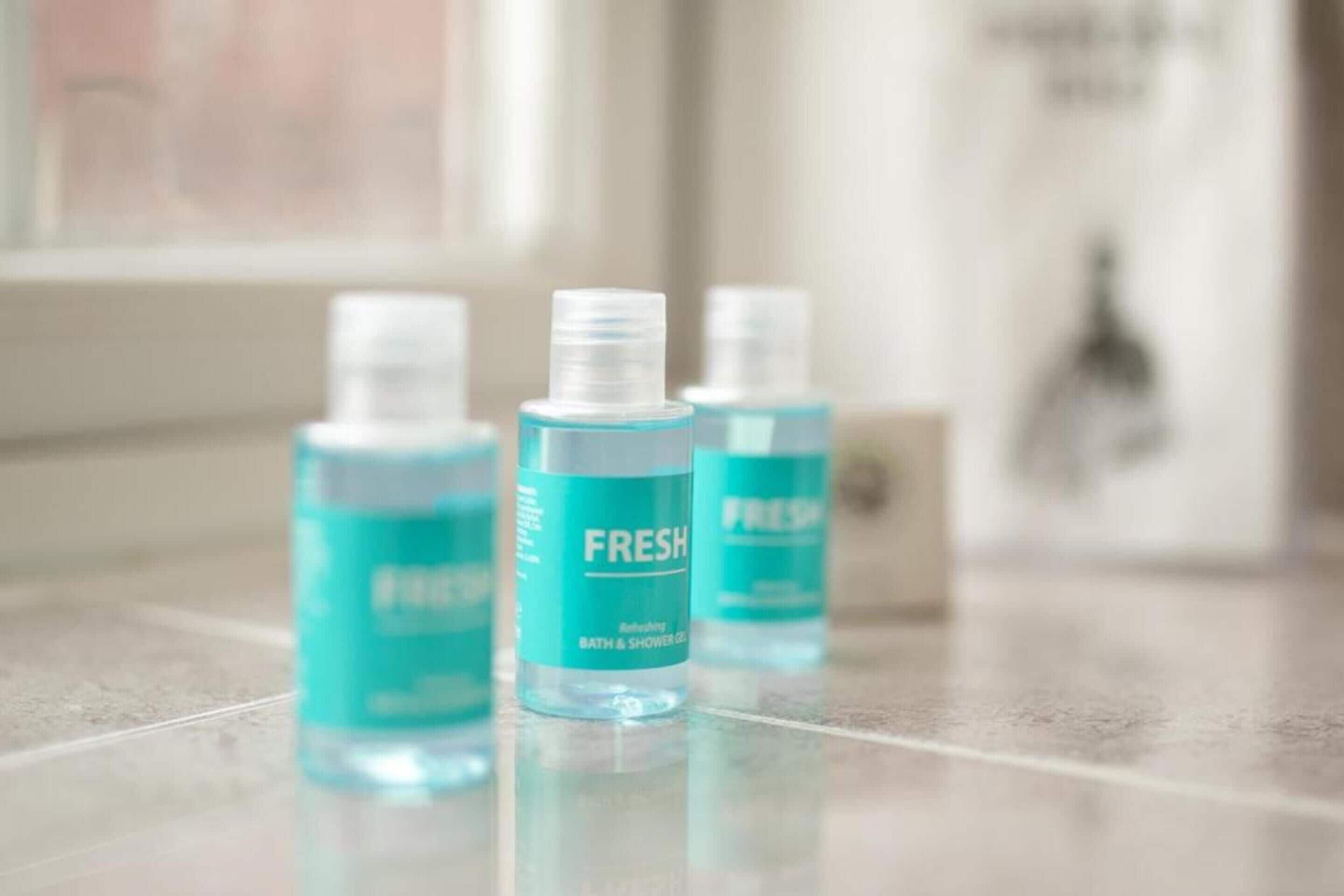 Tres botellas de gel de baño y ducha 'FRESH' sobre una superficie reflectante.