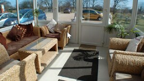 A sunroom with wicker furniture, large windows, and a view of parked cars outside.