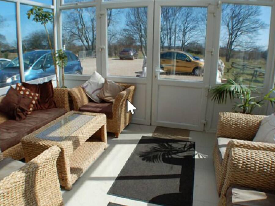 A sunroom with wicker furniture, large windows, and a view of parked cars outside.