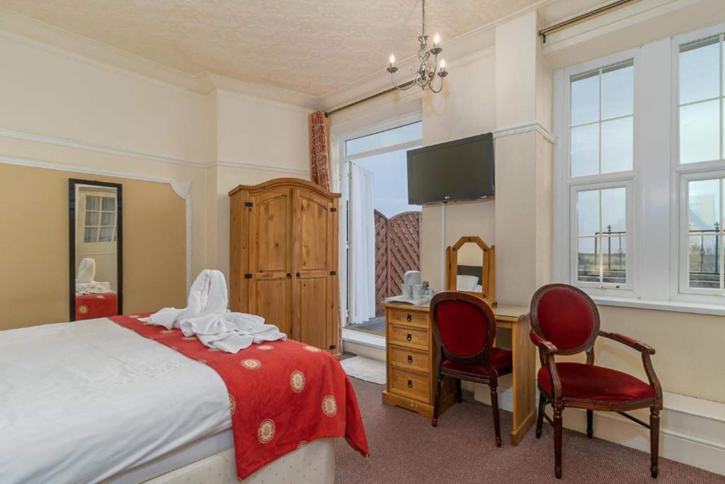 A hotel room with a bed, a wooden wardrobe, a desk with a chair, a television, and a window with a view.