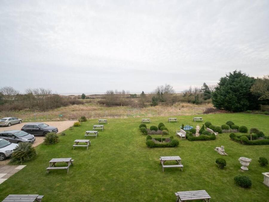 A spacious outdoor area with multiple picnic tables and a parking lot with several cars.