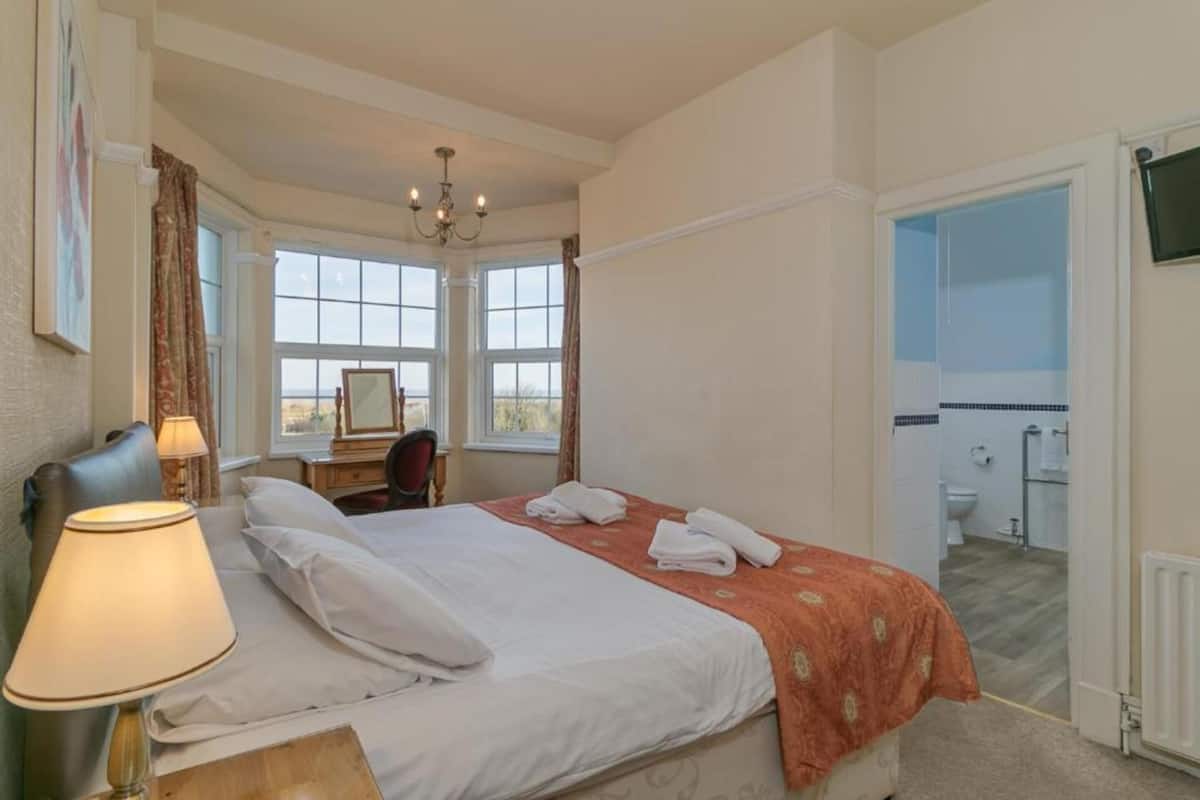 Une chambre d’hôtel avec un lit, un bureau, une chaise, une lampe et une vue sur la salle de bain.